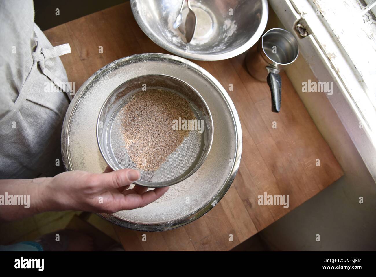 Una femmina cuoce in grembiule setola la farina in una ciotola di metallo. Preparazione per creare un impasto per la cottura. Patisserie fatta in casa. Foto di alta qualità Foto Stock