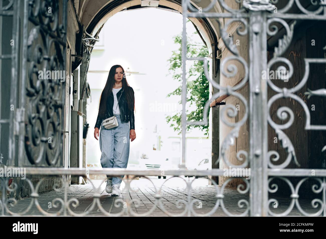 Giovane donna con capelli lunghi uscendo da vecchio edificio vintage attraverso la porta di vetro ornata per la strada di una grande città. San Pietroburgo, Russia. Foto Stock