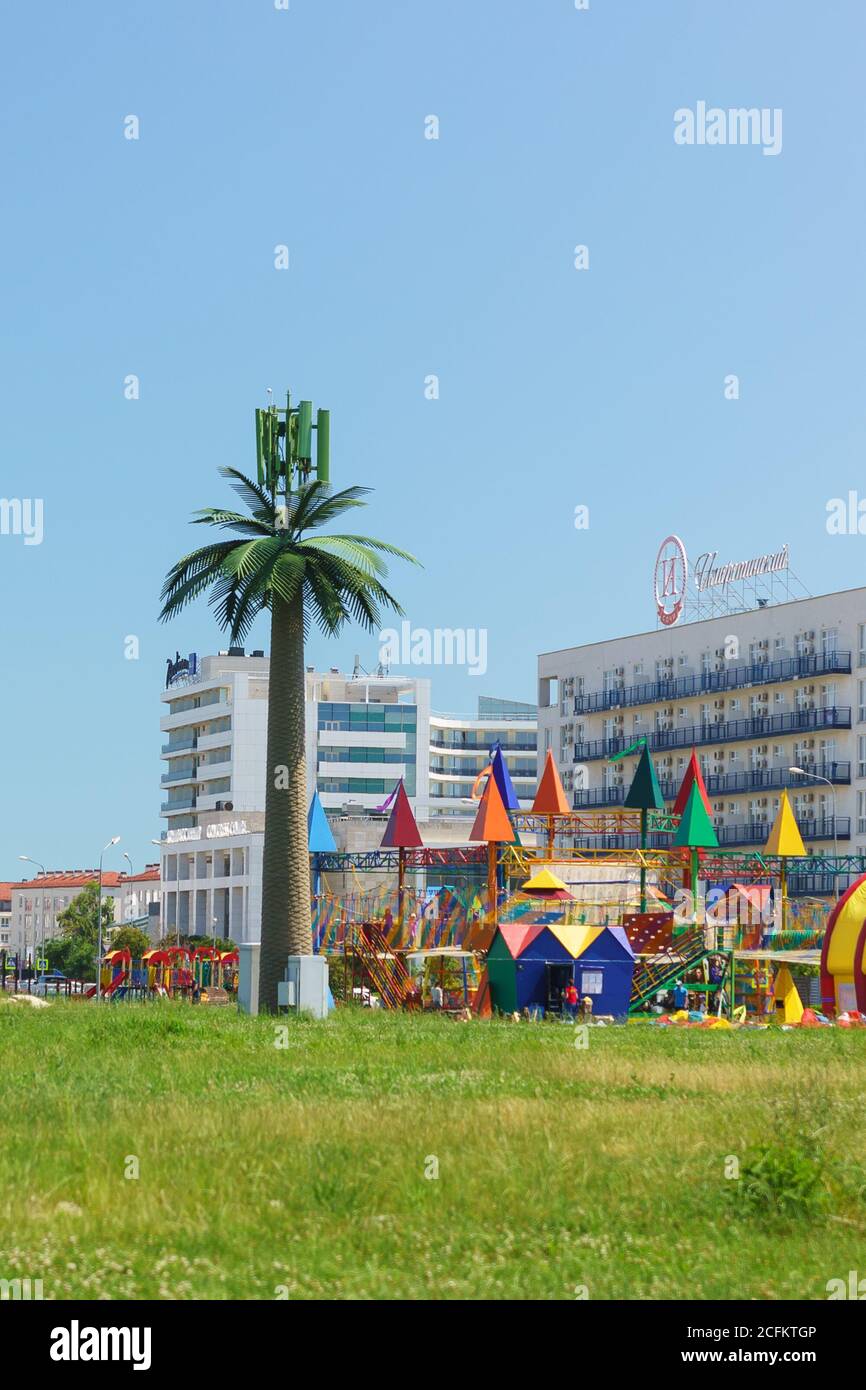 Russia, Sochi, regione di Krasnodar - Giugno 08.2017: Una torre cellulare travestita come una palma nei pressi di un parco giochi per bambini Foto Stock