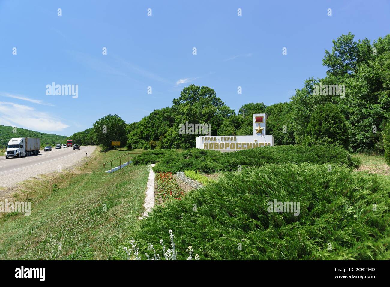 Russia, regione di Krasnodar, autostrada federale A146 'Krasnodar - Verkhnebakansky' - 12 giugno 2018: Stele alla strada con traffico pesante circondato dal verde Foto Stock