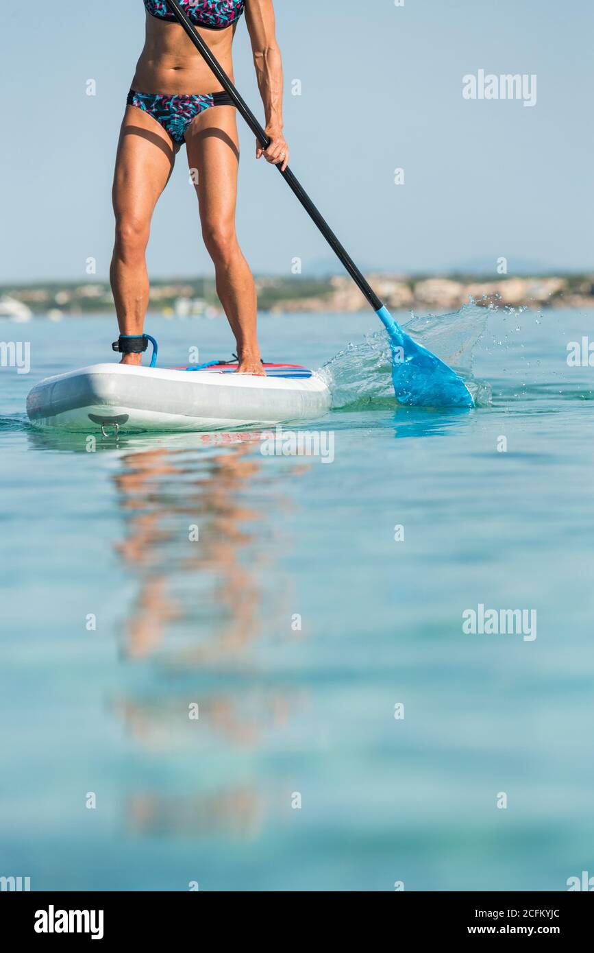 Crop anonimo surfer femminile in piedi su tavola da surf e canottaggio con  pagaia mentre si pratica sulla superficie del mare in estate Foto stock -  Alamy