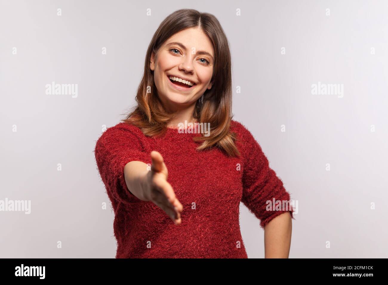 Ciao! Ritratto di felice amichevole bruna ragazza in maglione shaggy che offre handshake, familiarizzare, sorridendo amichevole, espressione ospitale. indo Foto Stock