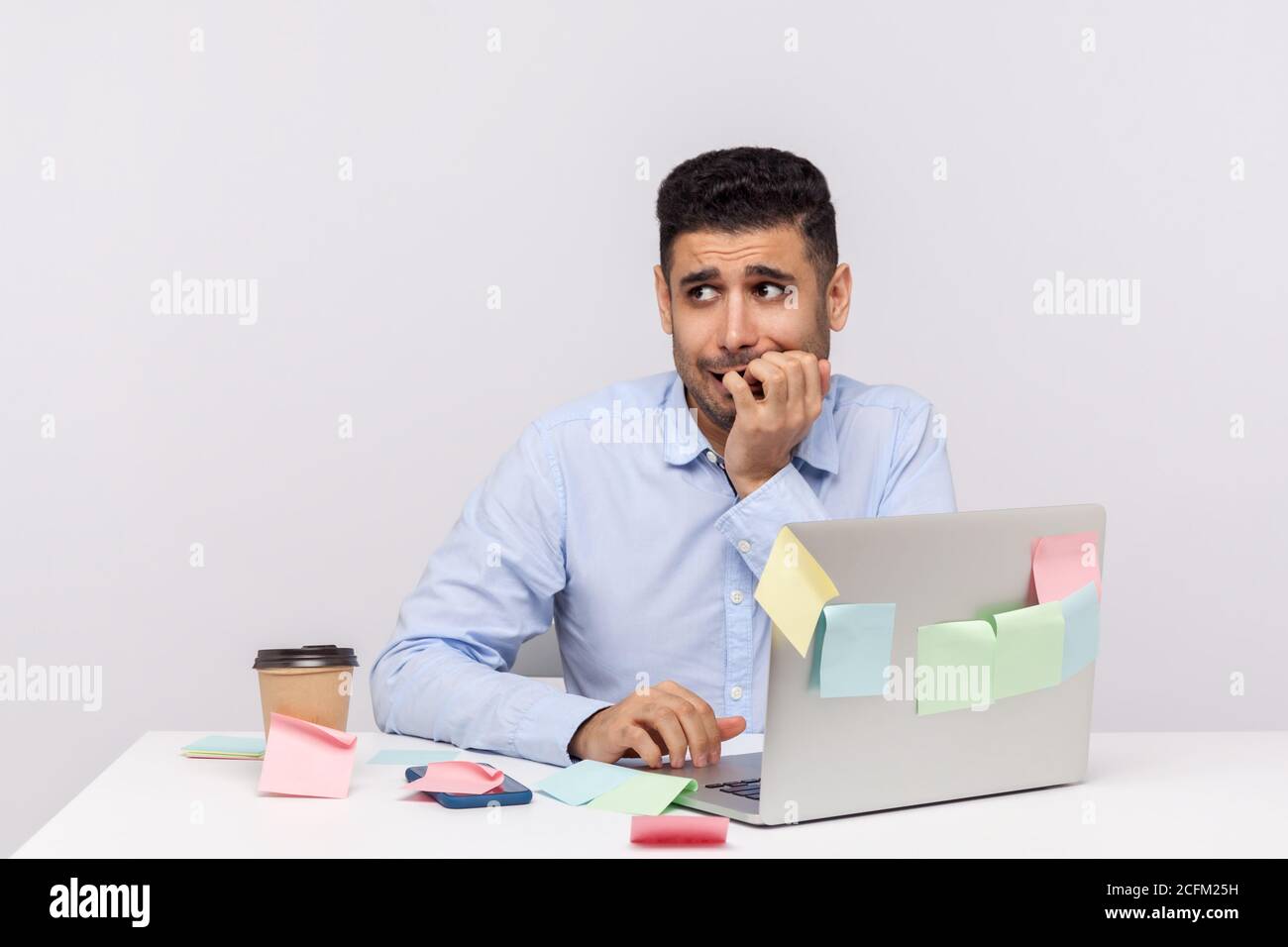 Disturbo d'ansia, lavoro stressante. Infelice dipendente uomo frustrato seduto in ufficio con note appiccicose tutto intorno, mordente unghie, nervou Foto Stock
