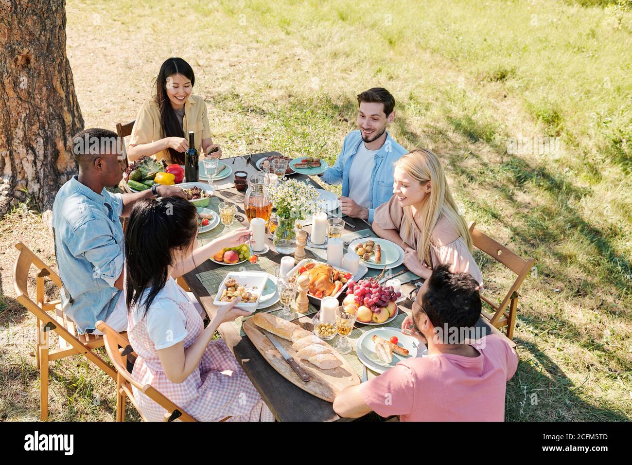 Gruppo di giovani amici felici riuniti dal tavolo servito con cibo fatto in casa Foto Stock