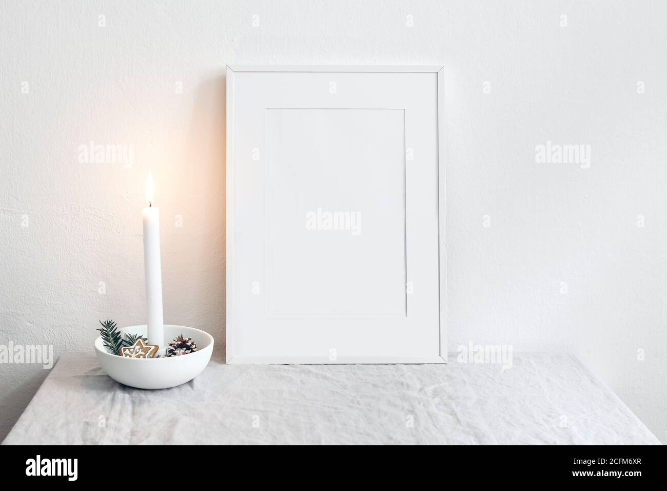 Cornice bianca mockup scena. Natale stagionale natura morta. Candela che brucia in ceramica portacandele. Interni scandinavi. Stelle di pan di zenzero Foto Stock