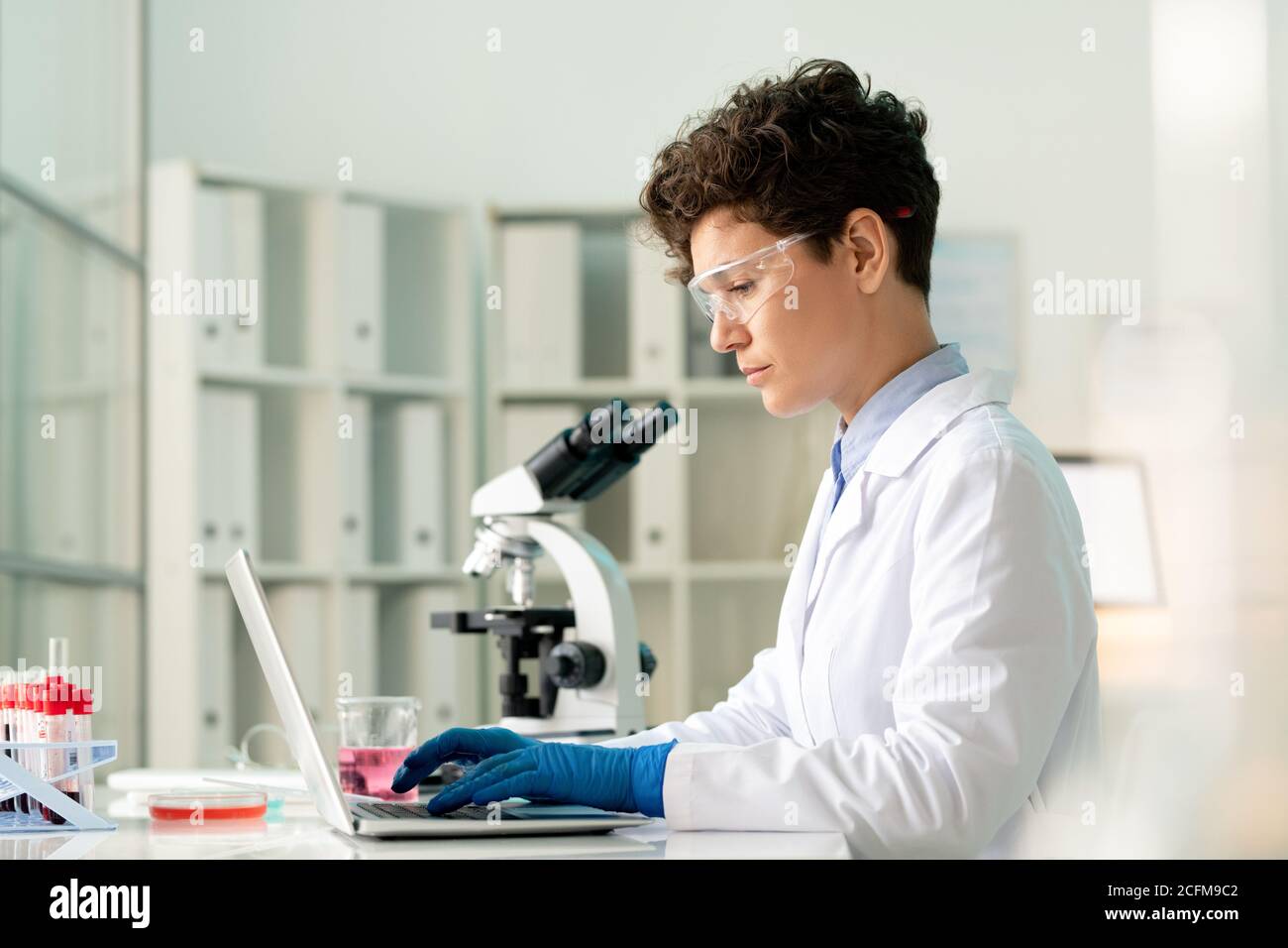 Un giovane e serio lavoratore di laboratorio seduto davanti al computer portatile e. immissione di dati scientifici Foto Stock