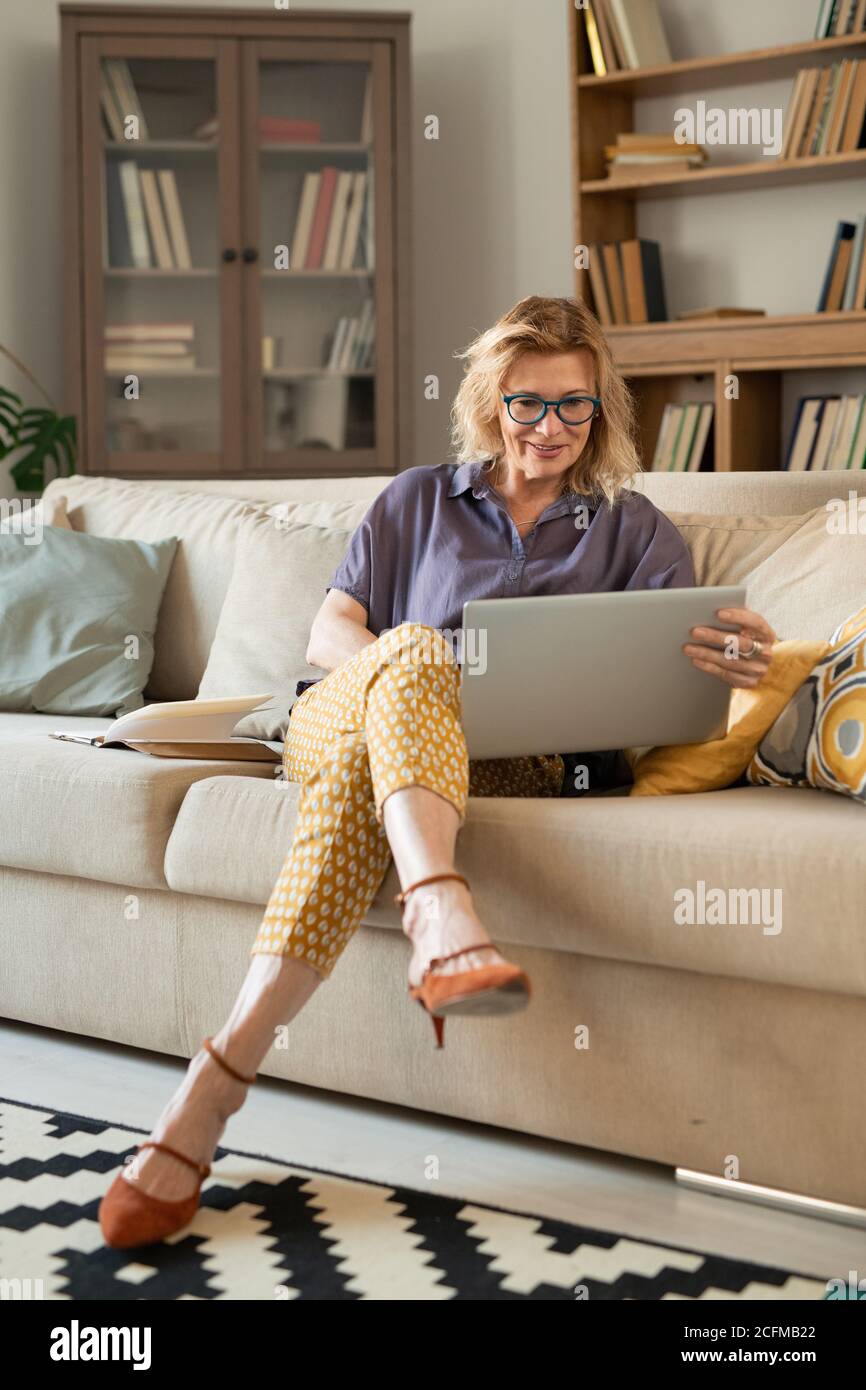 Donna d'affari bionda matura che guarda il display del tablet mentre si siede lettino Foto Stock