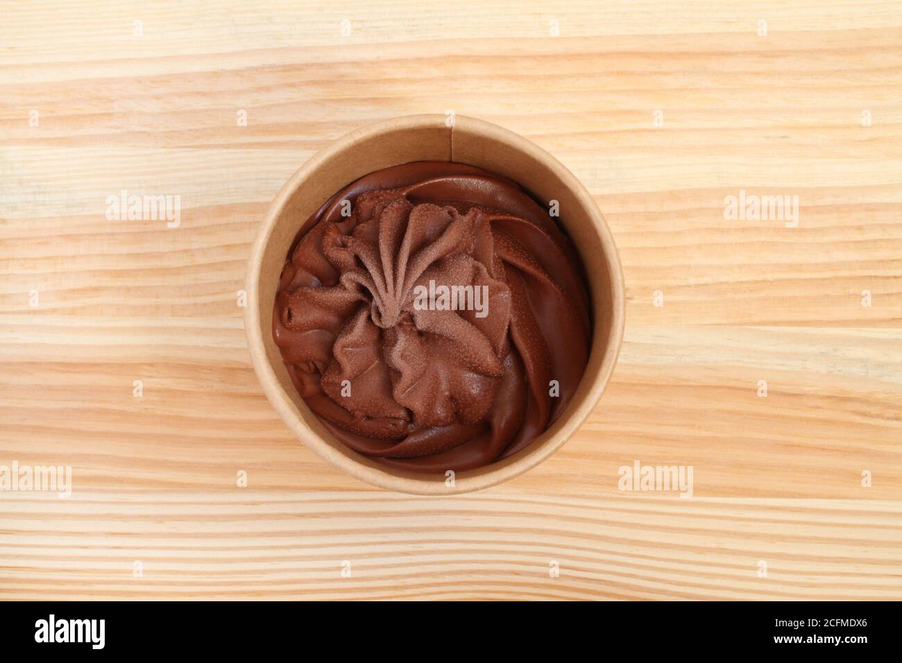 Il gelato al cioccolato in una tazza di cartone si trova su un tavolo di legno. Primo piano. Vista dall'alto verso il basso Foto Stock