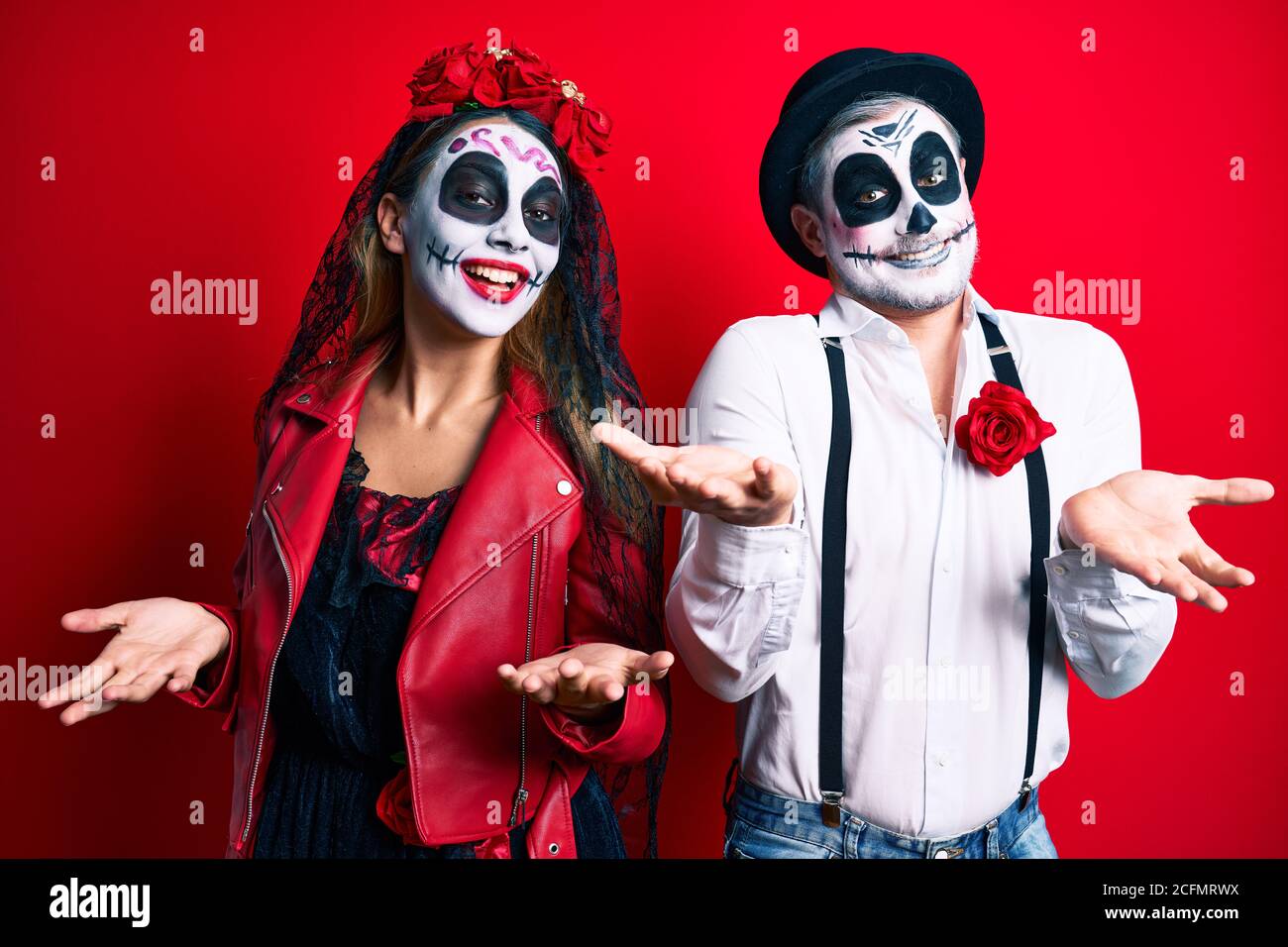 Coppia indossando giorno del costume morto sopra rosso sorridente allegro a braccia aperte come cordiale benvenuto, positivi e fiduciosi saluti Foto Stock