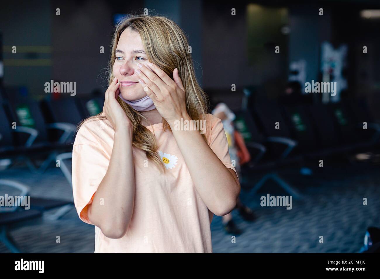 Ragazza che indossa una maschera di protezione per coronavirus o covid 19 sfregando il viso con mani sporche in aeroporto. Non toccare il viso. Spazio di copia. Foto Stock