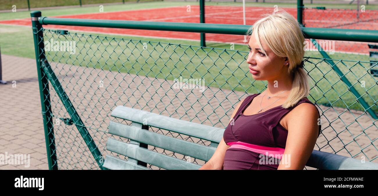 Il giocatore di tennis si appoggia sulla panchina del campo da tennis. Ritratto di sportivo su campo da tennis con terreno rosso. Vita sana. Banner. Spazio di copia. Foto Stock