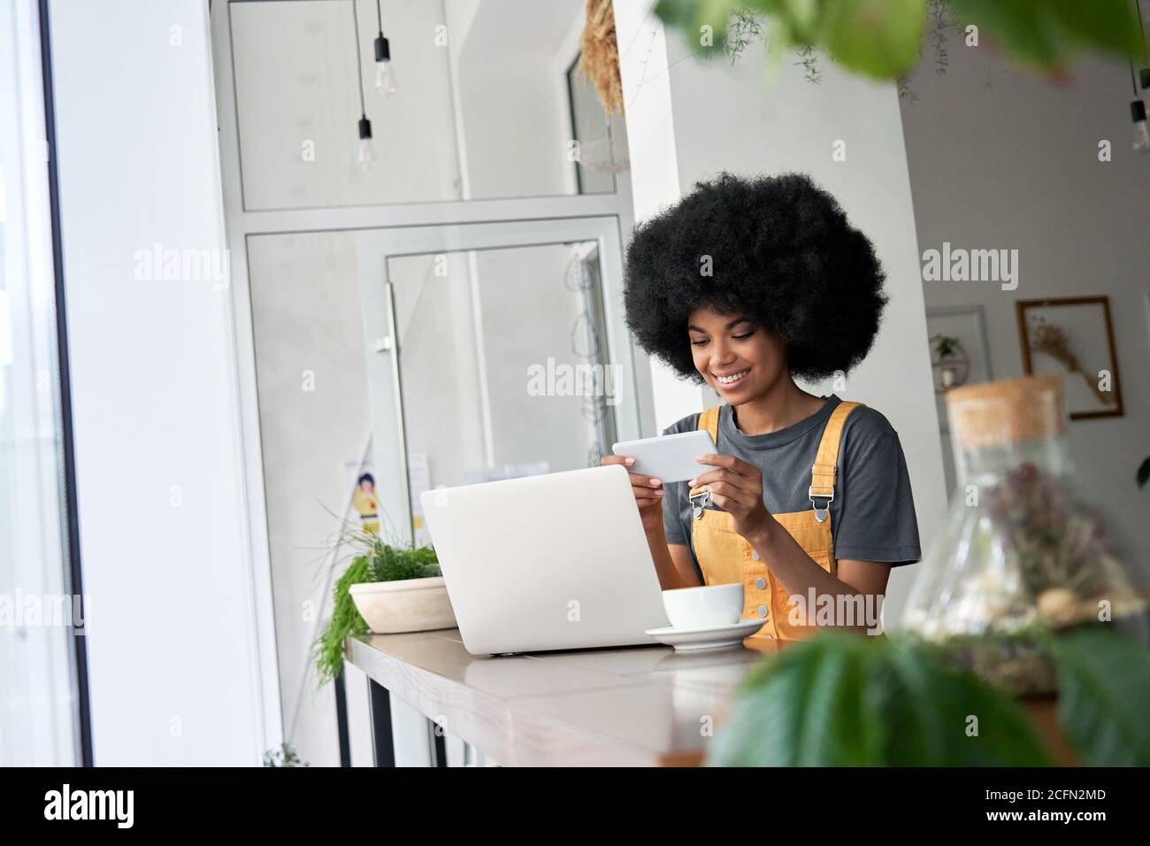 Una donna africana sorridente studentessa che guarda l'annuncio mobile al telefono seduto al tavolo del caffè. Foto Stock