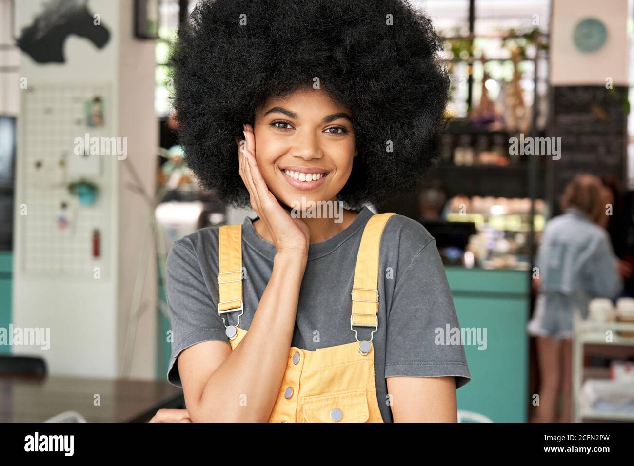 Donna africana felice con capelli afro guarda i supporti della macchina fotografica nel caffè, headshot. Foto Stock