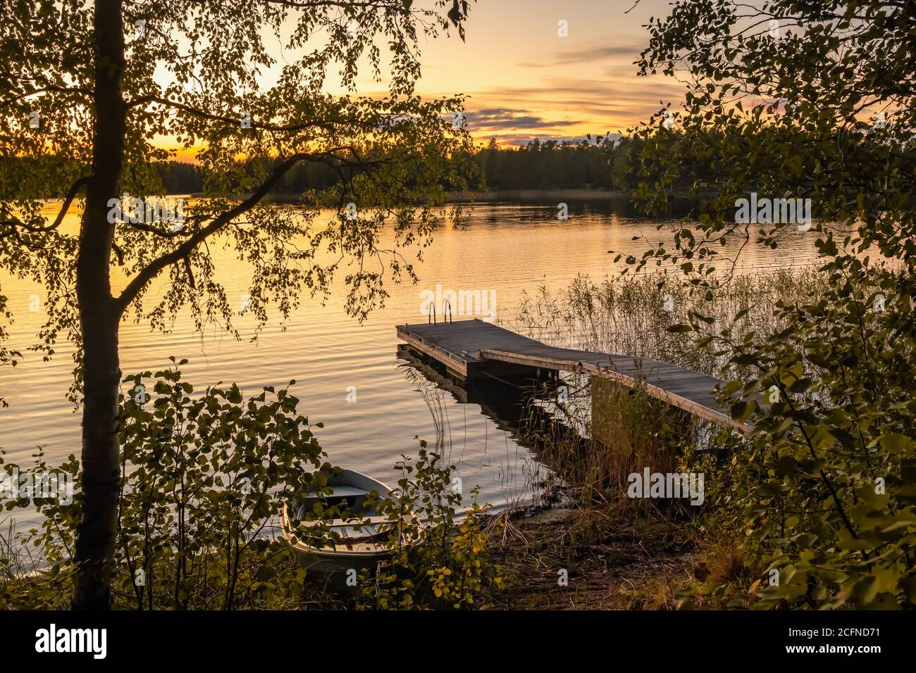 Molo di legno e piccola barca in un lago tranquillo a. Tramonto in Finlandia Foto Stock