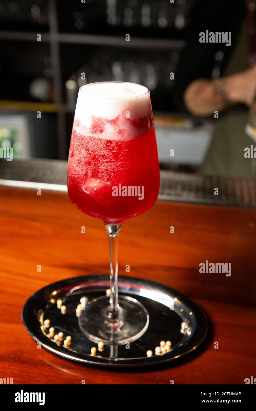 Dolce cocktail freddo di colore rosso si erge su un tavolo di legno in un pub. Foto Stock