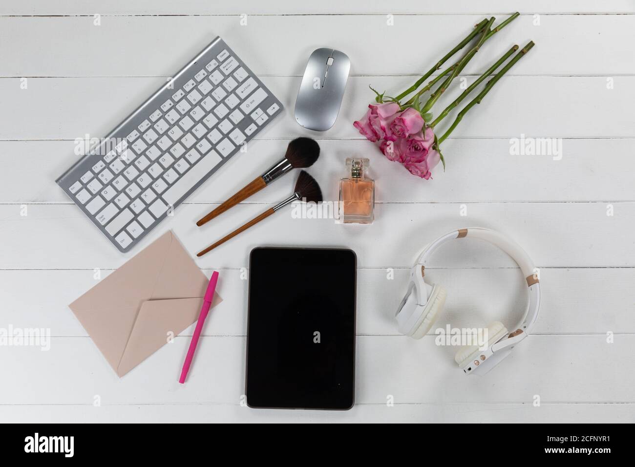 Vista di una parola chiave con make up, tablet, fiori e cuffie su sfondo di legno bianco Foto Stock