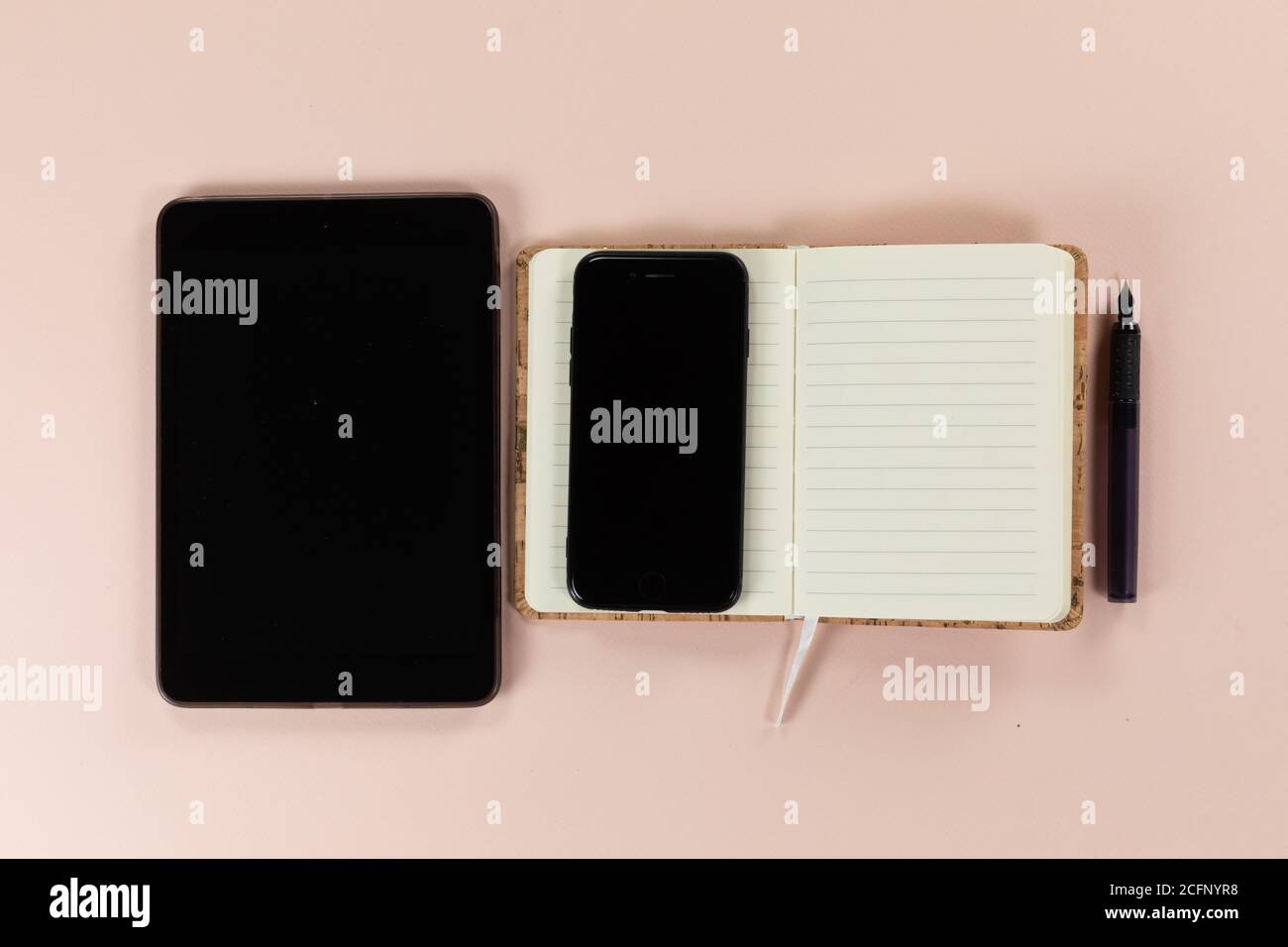 Visualizzazione di un tablet e di un telefono con notebook e penna su sfondo rosa Foto Stock