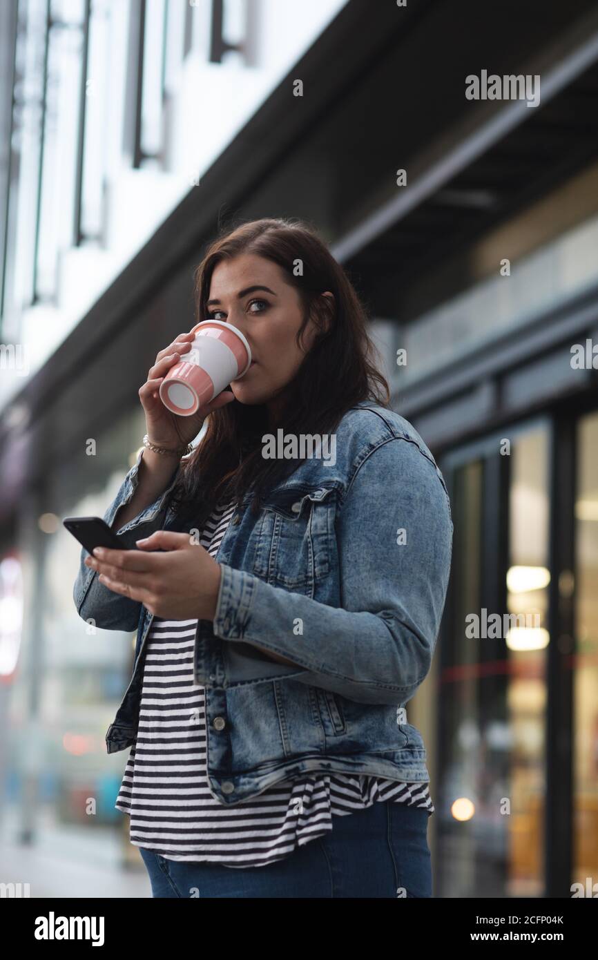 Donna caucasica curvilinea che beve un caffè da asporto in città Foto Stock