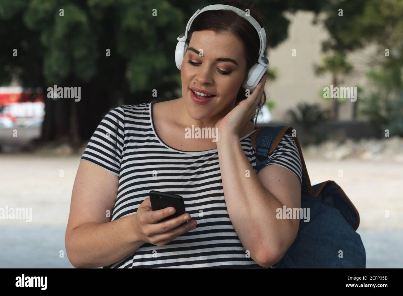 Donna caucasica curvilinea che ascolta la musica sul suo smartphone Foto Stock