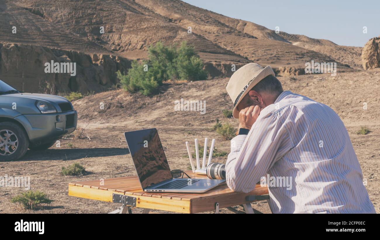 Uomo che lavora su un computer portatile all'aperto in montagna, facendo una breve pausa Foto Stock