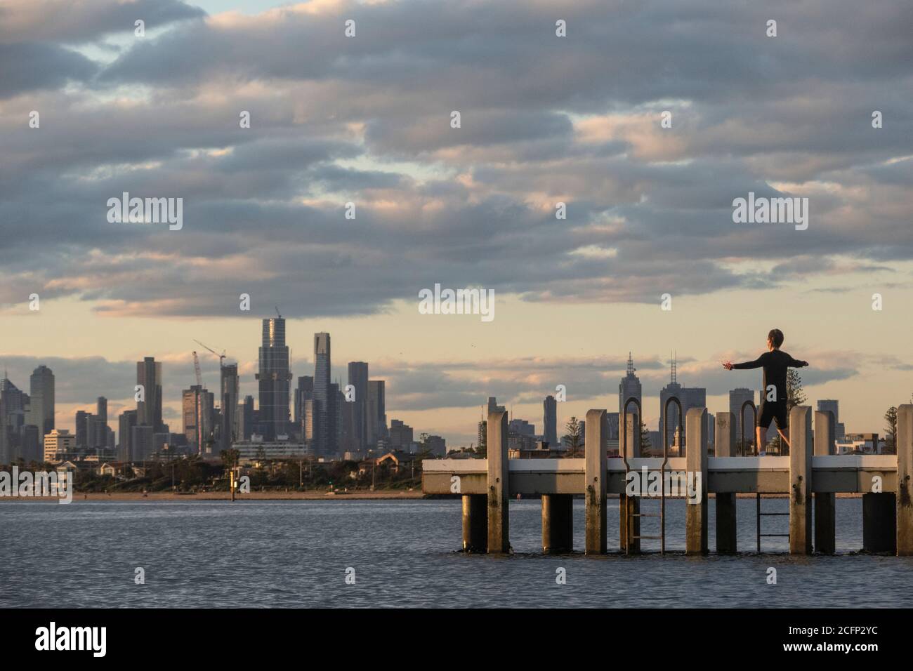 Melbourne Australia. Scene di vita quotidiana. Allenati su un molo a Port Phillip Bay con lo skyline di Melbourne sullo sfondo. Foto Stock