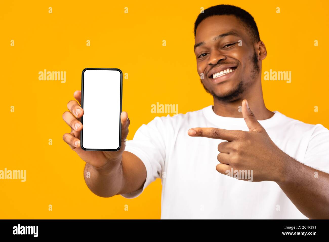 Uomo afroamericano che mostra la schermata del telefono cellulare, sfondo giallo, Mockup Foto Stock