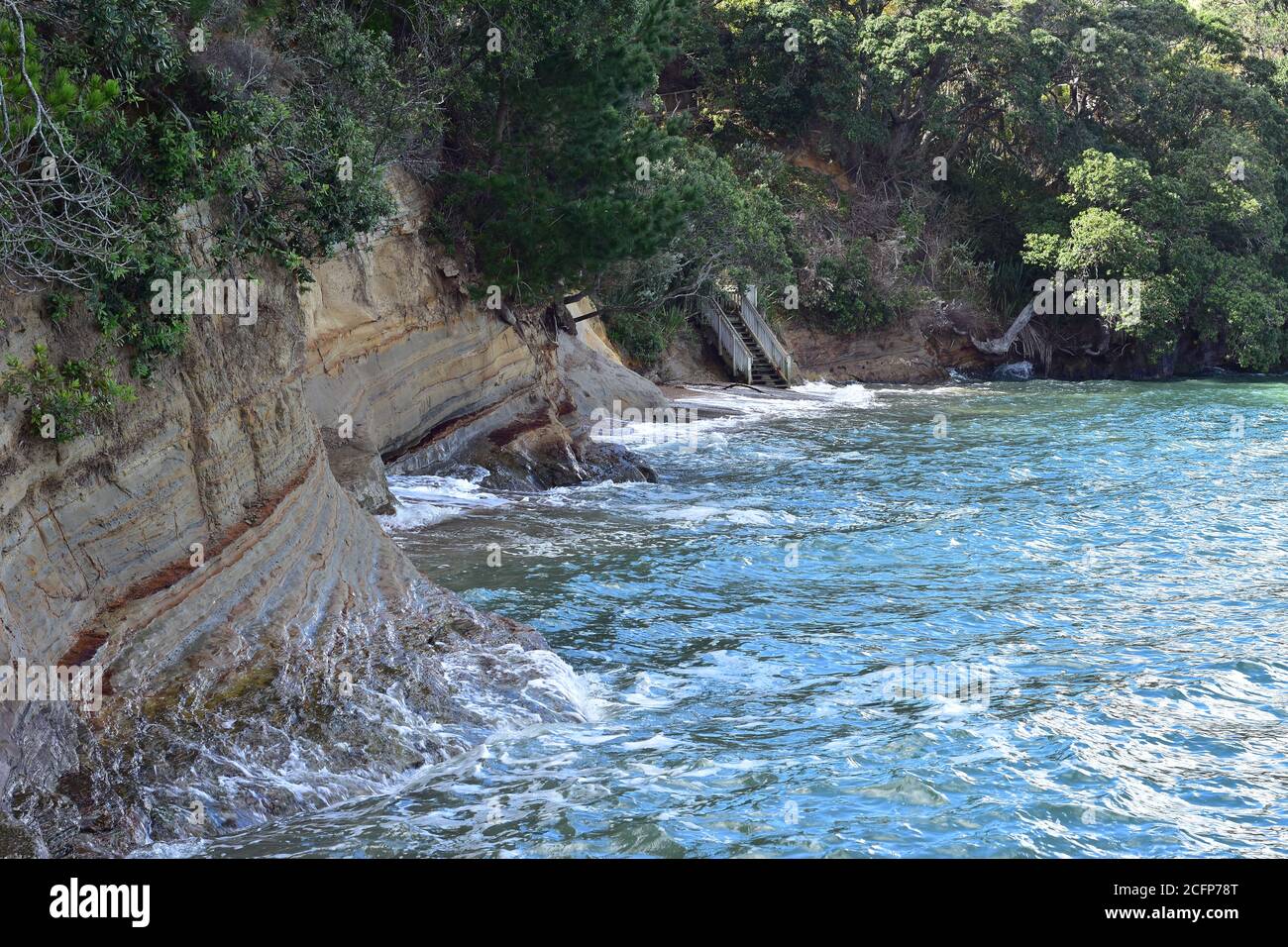 Onde di surf che toccano le scogliere costiere erodenti coperte di vegetazione durante l'alta marea. Foto Stock