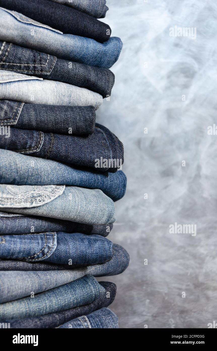 Pila di jeans piegati incautamente su sfondo grigio. Primo piano di jeans in diversi colori. Texture jeans o sfondo in denim. Spazio di copia Foto Stock