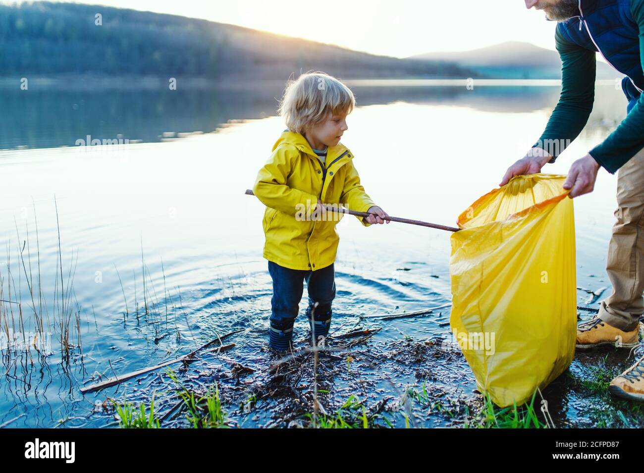 Padre con un piccolo figlio che raccoglie i rifiuti all'aperto in natura, pblogging concetto. Foto Stock