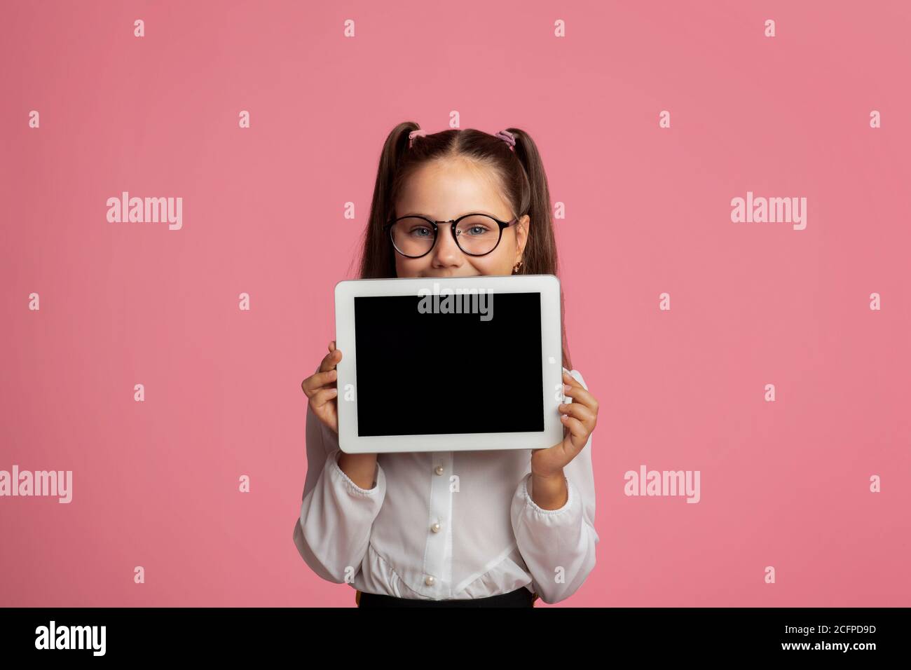 Istruzione e formazione a distanza per i bambini. Ragazza allegra in occhiali mostra tablet con schermo vuoto Foto Stock