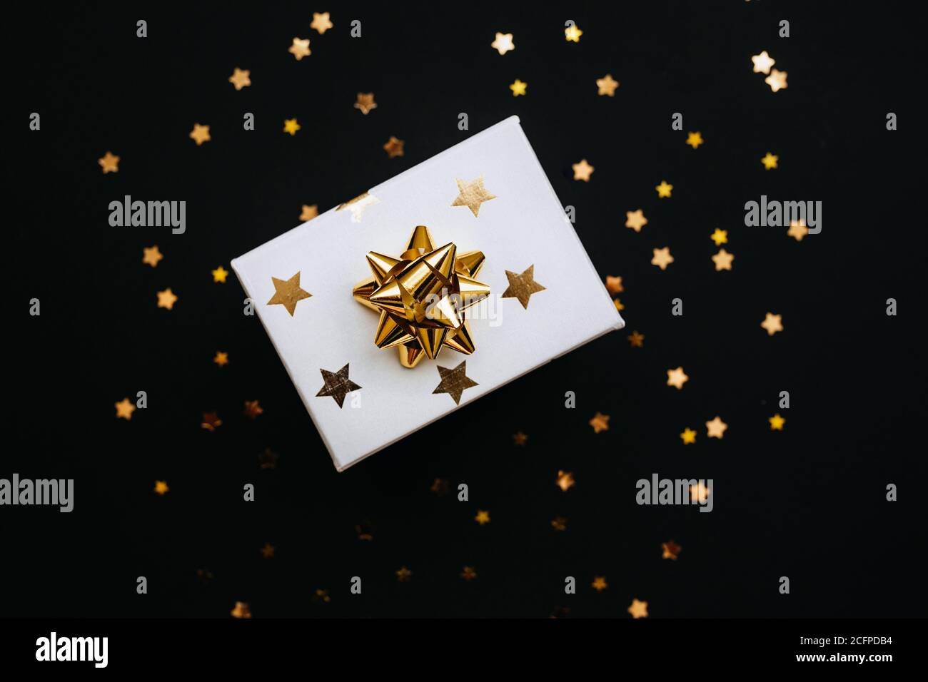 Confezione regalo natalizia con stelle dorate e arco su sfondo nero. Foto Stock