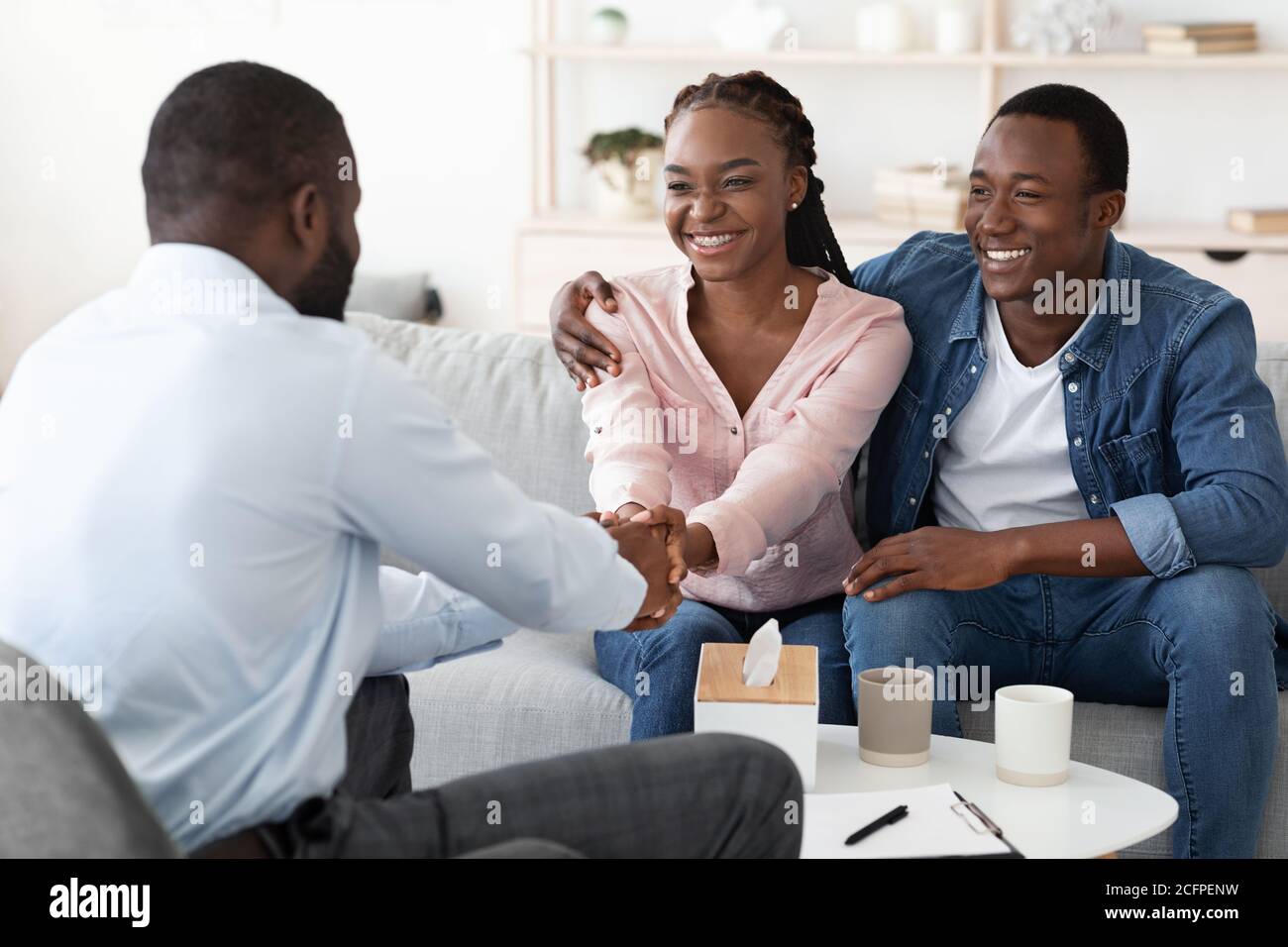 Riconciliazione del matrimonio. Felice coppia nera grata al consigliere di famiglia dopo la terapia riuscita Foto Stock