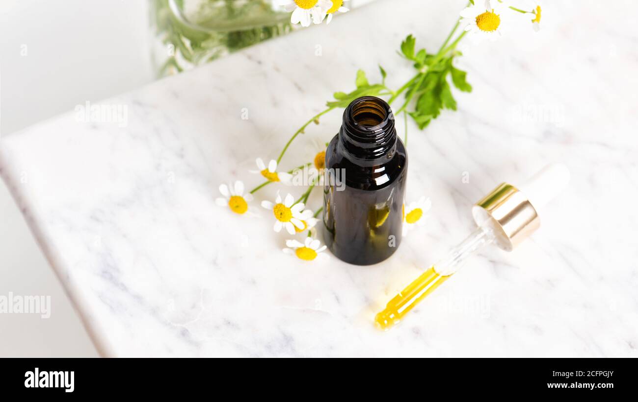 Bottiglia di essenza o siero di vetro marrone con camomilla fiori Foto Stock
