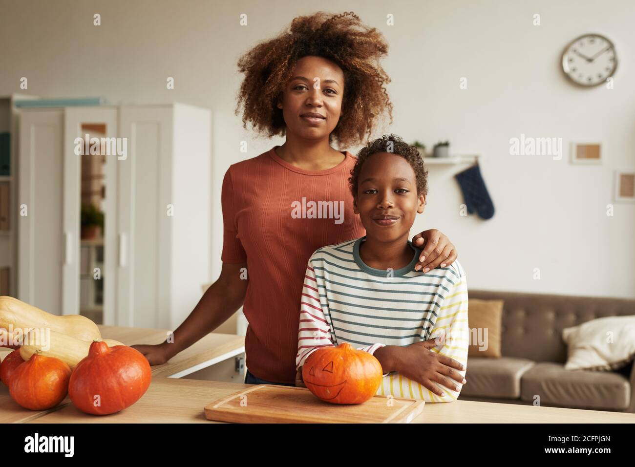 Bella donna afroamericana e suo figlio teen in piedi insieme a tavola con le zucche per la carvatura su di esso Foto Stock