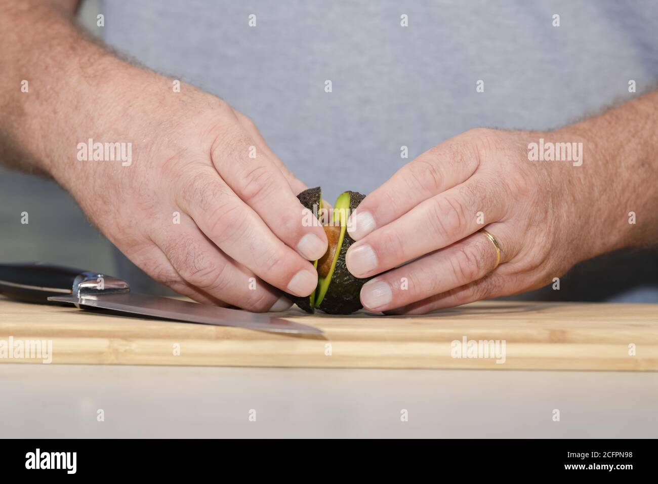 Primo piano delle mani maschili che separano le due metà di un avocado appena tagliato su un tagliere di legno Foto Stock