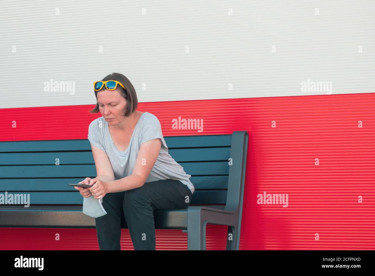 Donna che digita un messaggio di testo sul telefono cellulare e indossa un dispositivo di protezione maschera facciale intorno al polso in un nuovo concetto normale Foto Stock