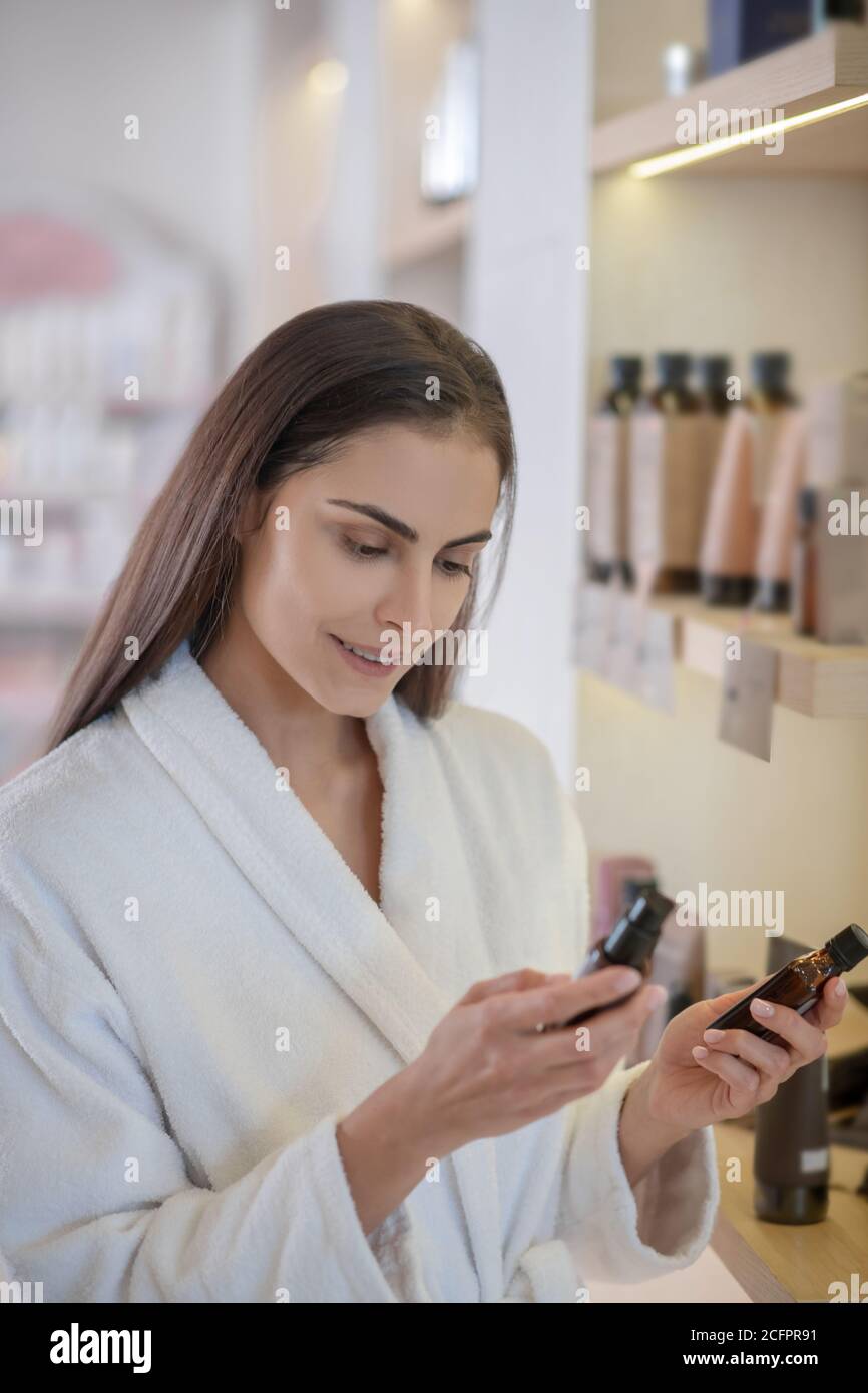 Donna in accappatoio bianco scegliendo prodotti per la cura di bellezza e. aspetto interessato Foto Stock