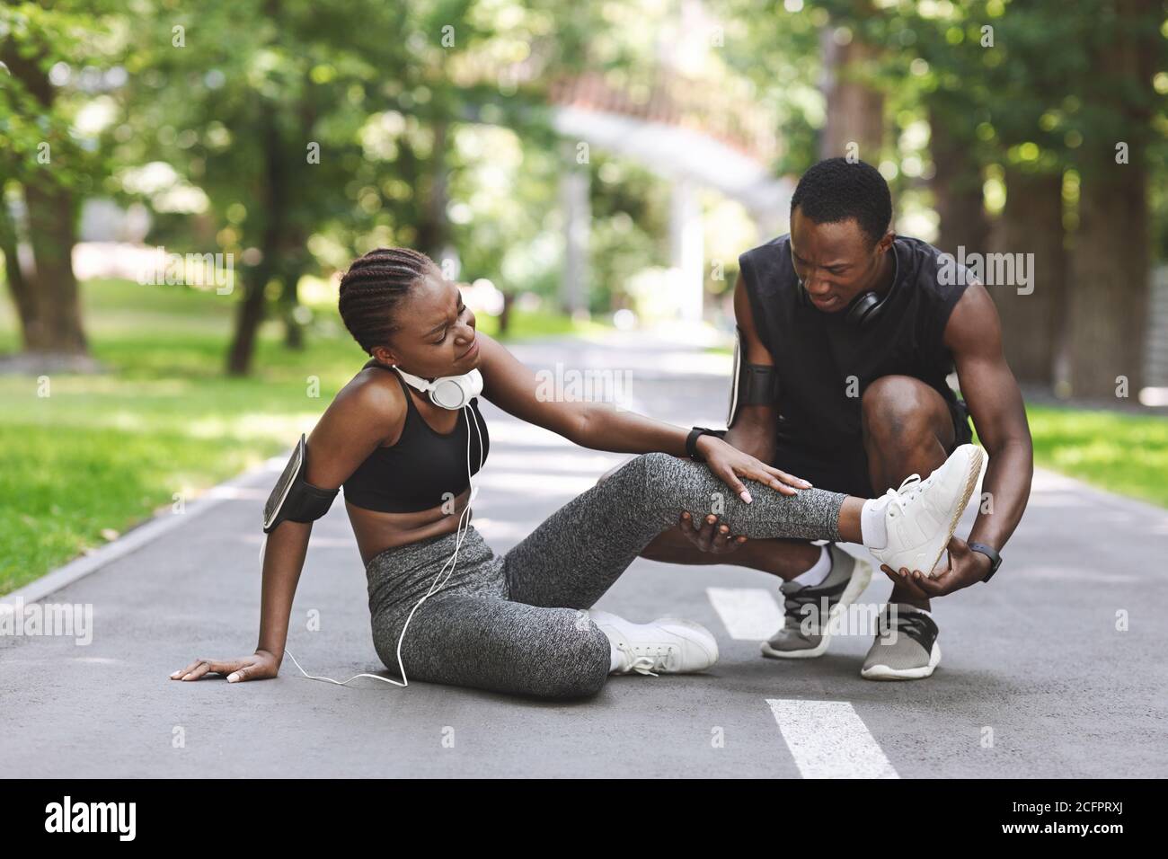 Caring Black Man massaggiando la gamba ferita della ragazza dopo la corsa Insieme all'aperto Foto Stock