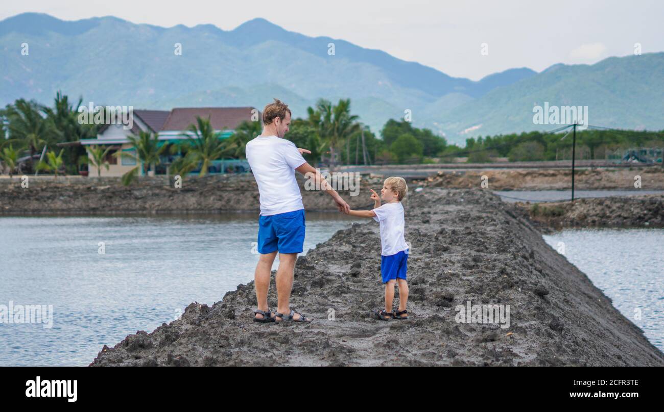 Padre figlio cammina vicino al lago di montagna, guarda il punto l'un l'altro, winking giocando. Felice infanzia. Home educazione naturale del bambino, giorno dei padri, papà Foto Stock