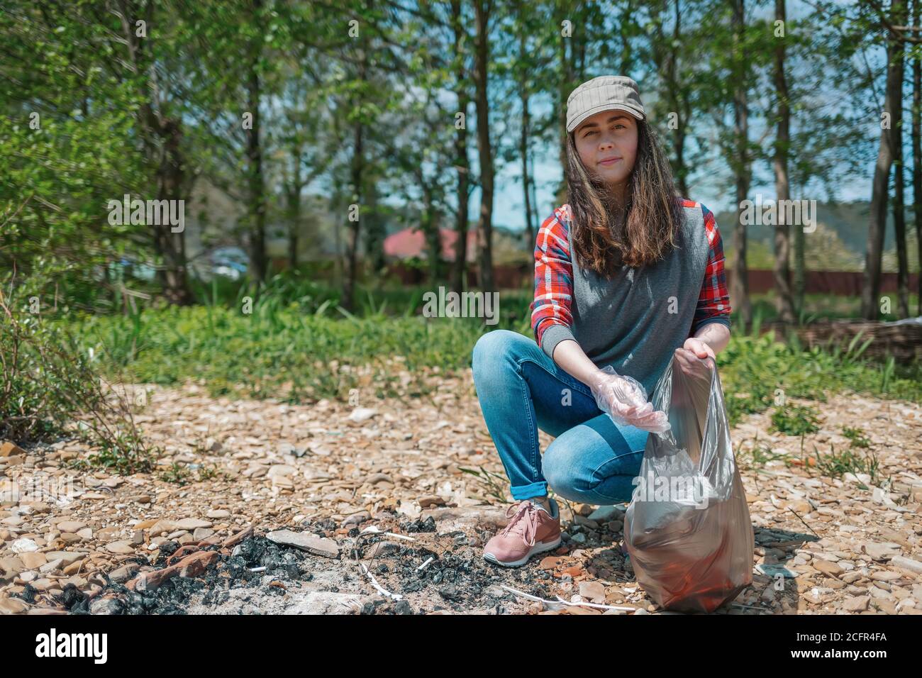 Una giovane volontaria femminile raccoglie i rifiuti nell'area pic-nic. Il concetto di giorno della terra e di ecologia e conservazione ambientale. Foto Stock