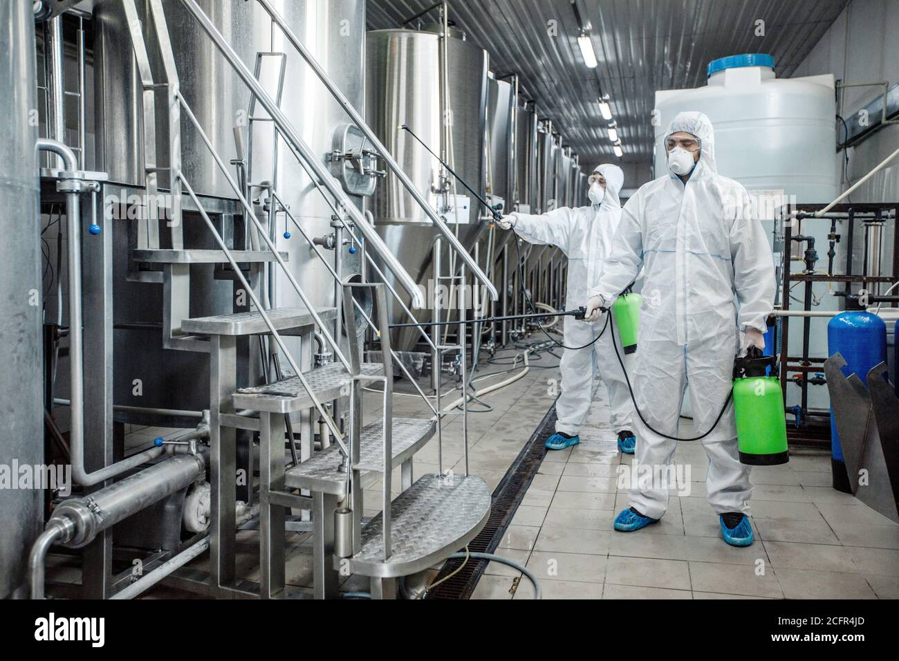 Uomini in tute di protezione con sacchetti spray verdi disinfettare pianta Foto Stock