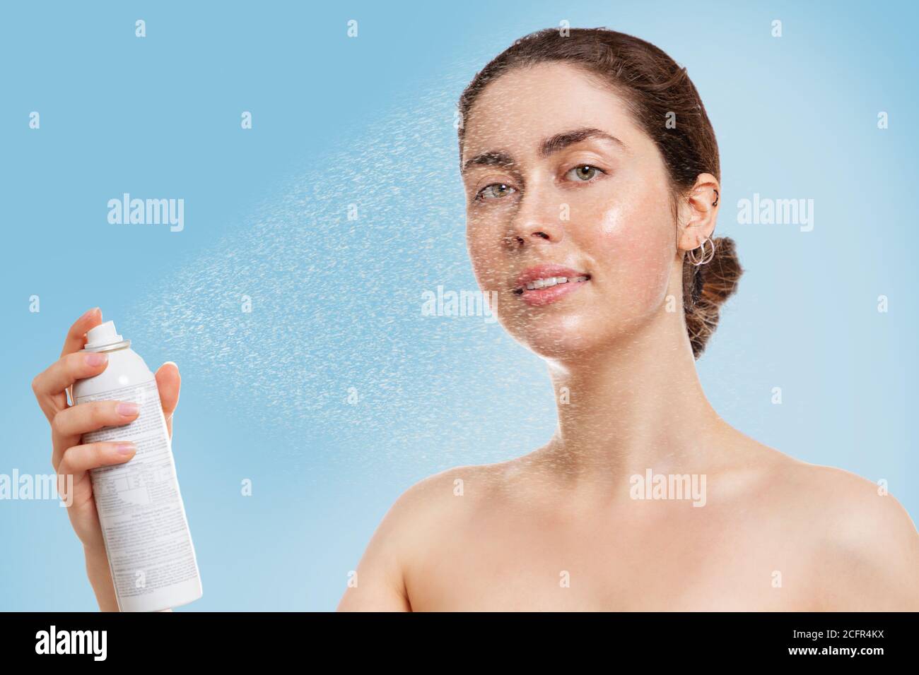 Ritratto di giovane caucasica con pelle bagnata spruzzi d'acqua termale sul viso. Sfondo blu. Concetto di cosmetologia, cura della pelle e idratazione Foto Stock