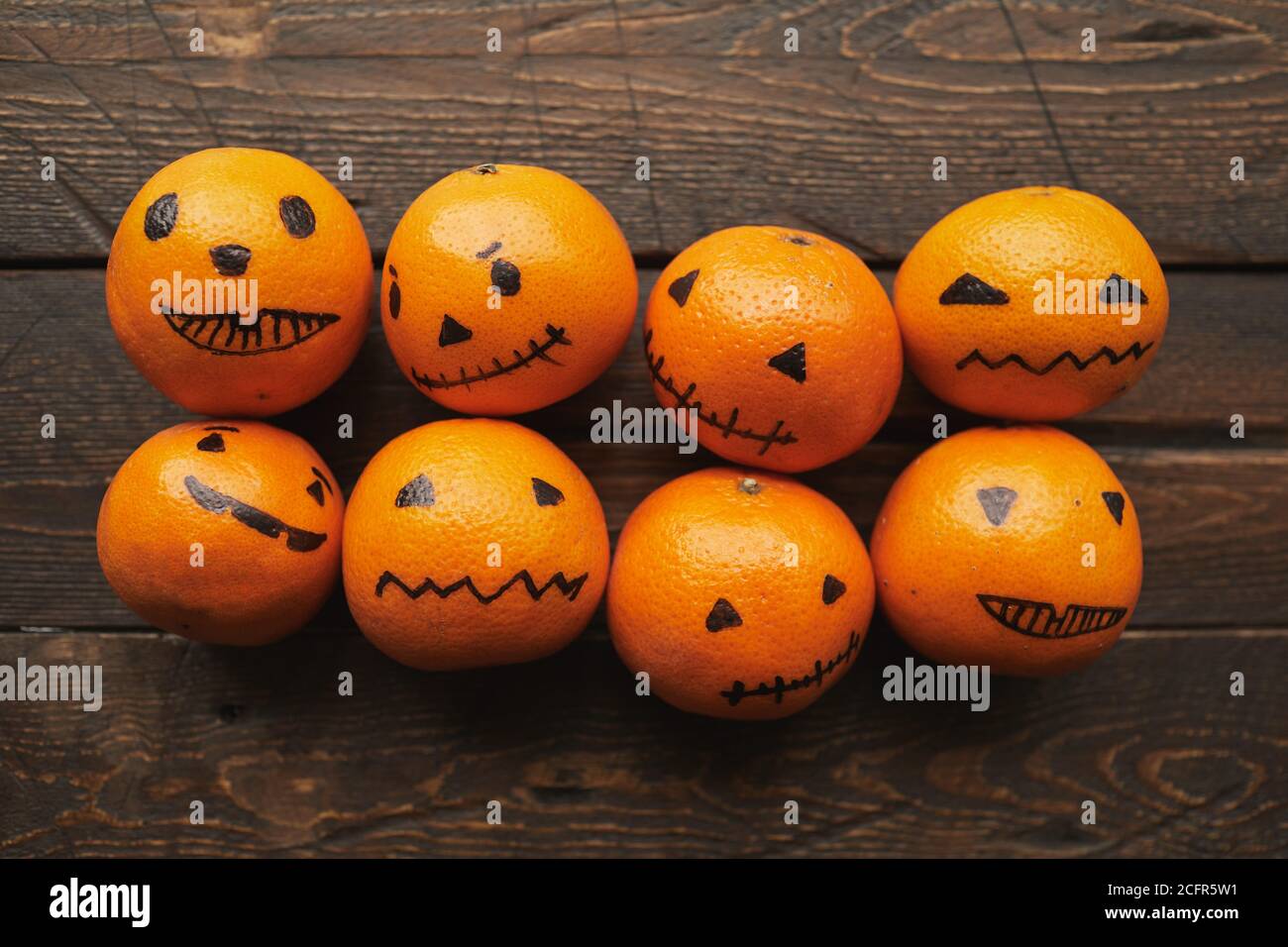 Gruppo di tangerini arancioni con jack o' lanterna facce disegnate su di loro giacenti su un tavolo di legno marrone scuro, piatto Foto Stock