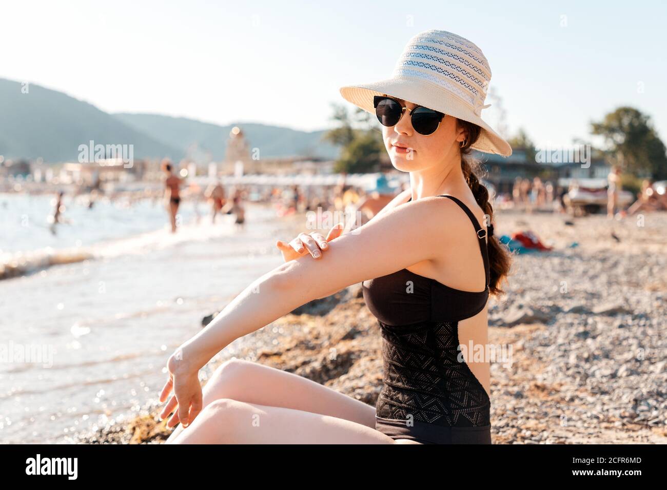 Una donna in un cappello di paglia, costume da bagno e occhiali spalmare  crema solare seduta sulla spiaggia. Il concetto di abbronzatura adeguata  Foto stock - Alamy