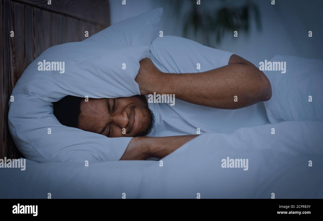 L'uomo africano copre le orecchie con il cuscino che ha l'Insomnia a casa Foto Stock