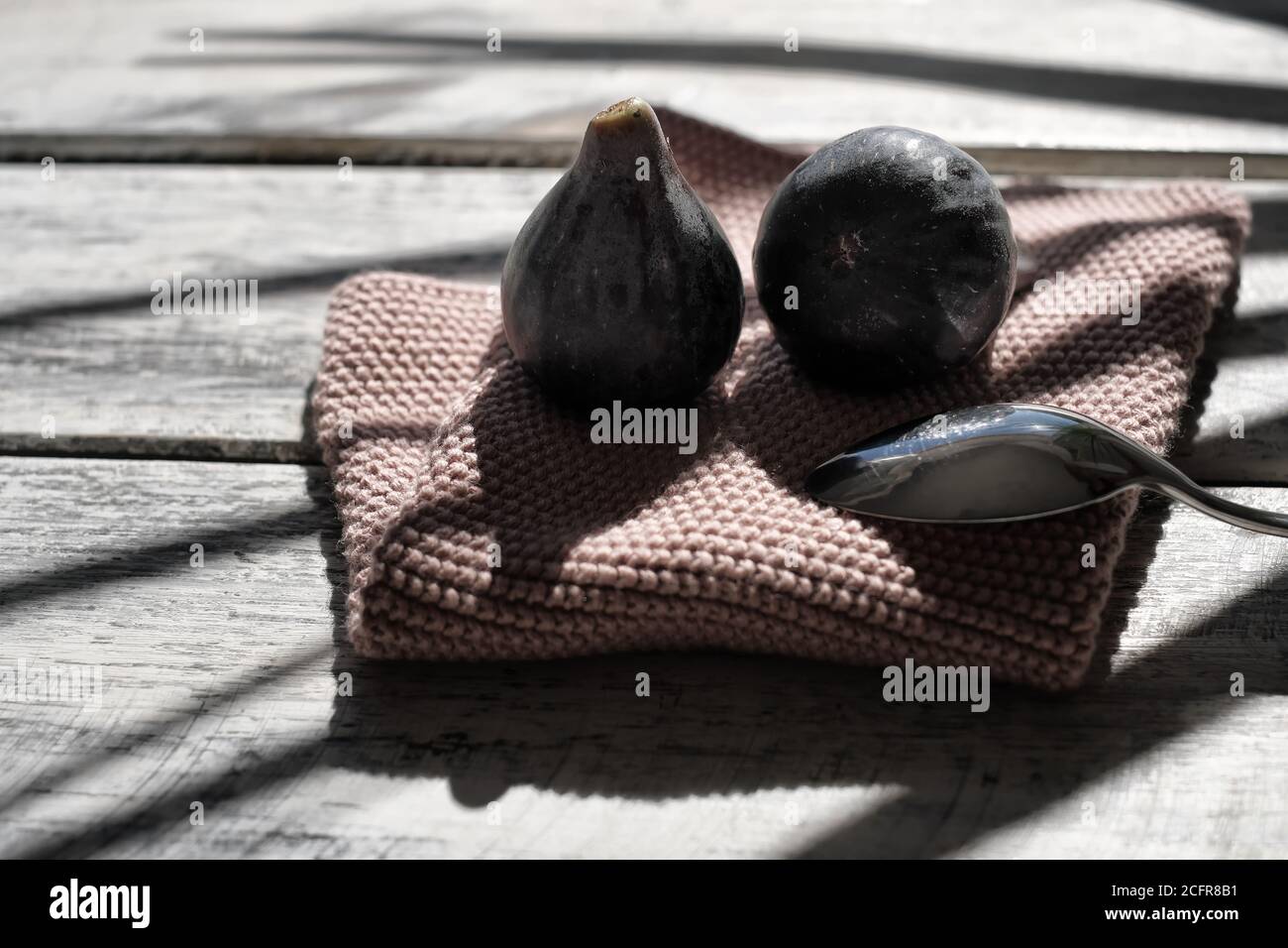 fichi maturi ben disposti su un elegante tavolo in legno bianco su un vecchio tovagliolo rosa, ombre dure di una palma Foto Stock