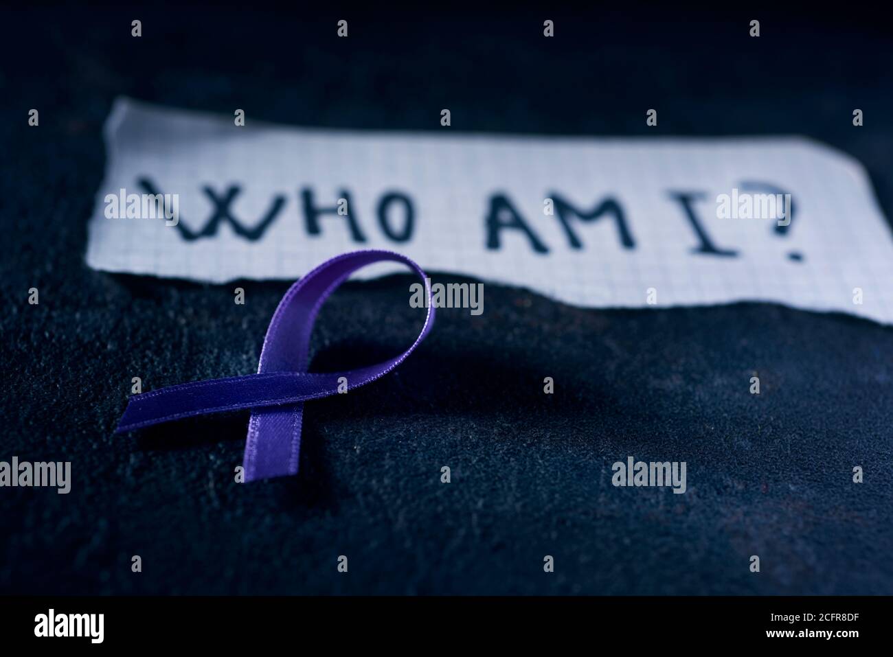 Un nastro di consapevolezza viola, per la consapevolezza della malattia di Alzheimers, e un pezzo di carta con la domanda che sono scritto in esso, su una carta di colore nero Foto Stock