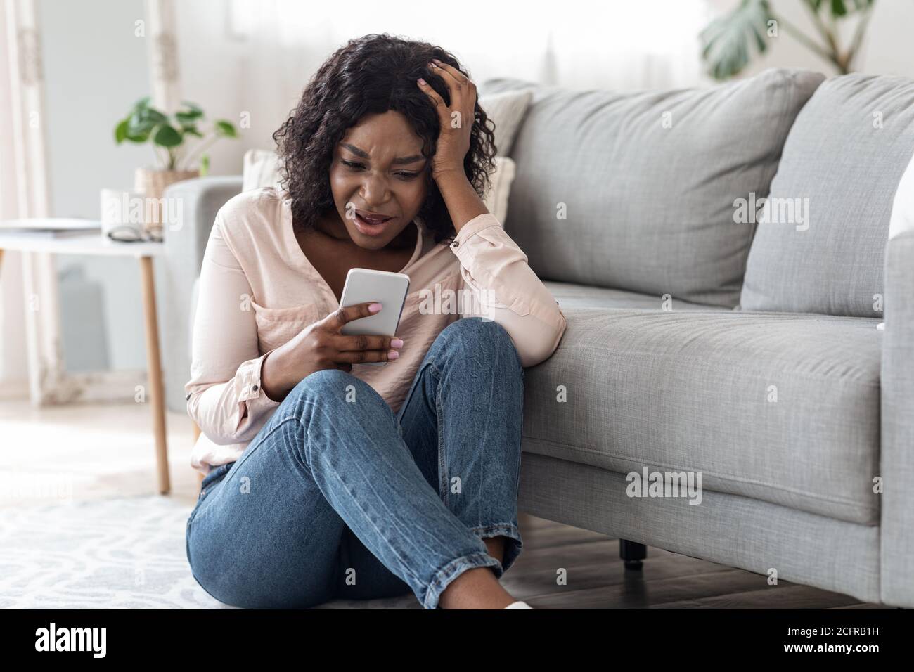 Cattive notizie. Sconvolto Afro Woman lettura messaggio sullo smartphone a casa Foto Stock