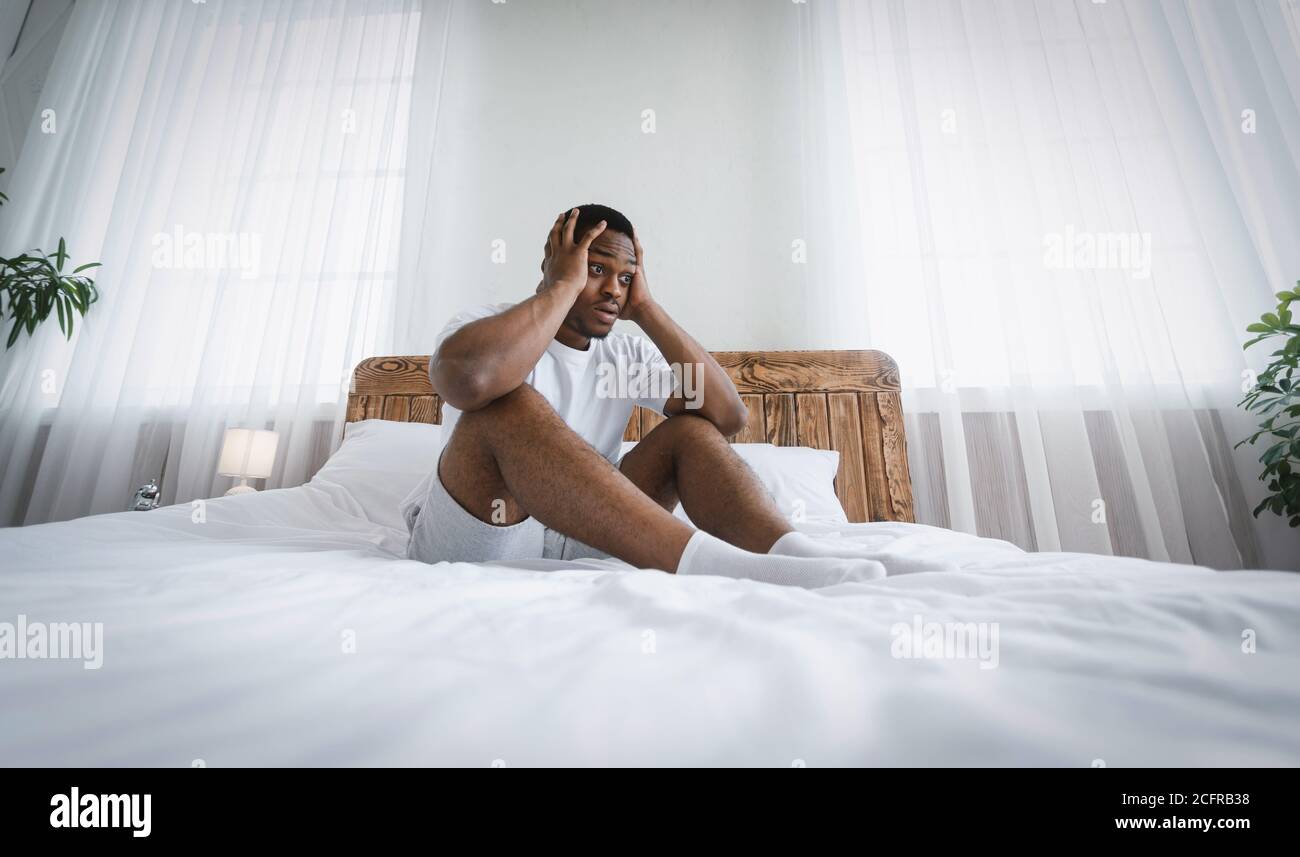 Stressato Black Millennial Guy seduto in letto toccando testa interna Foto Stock