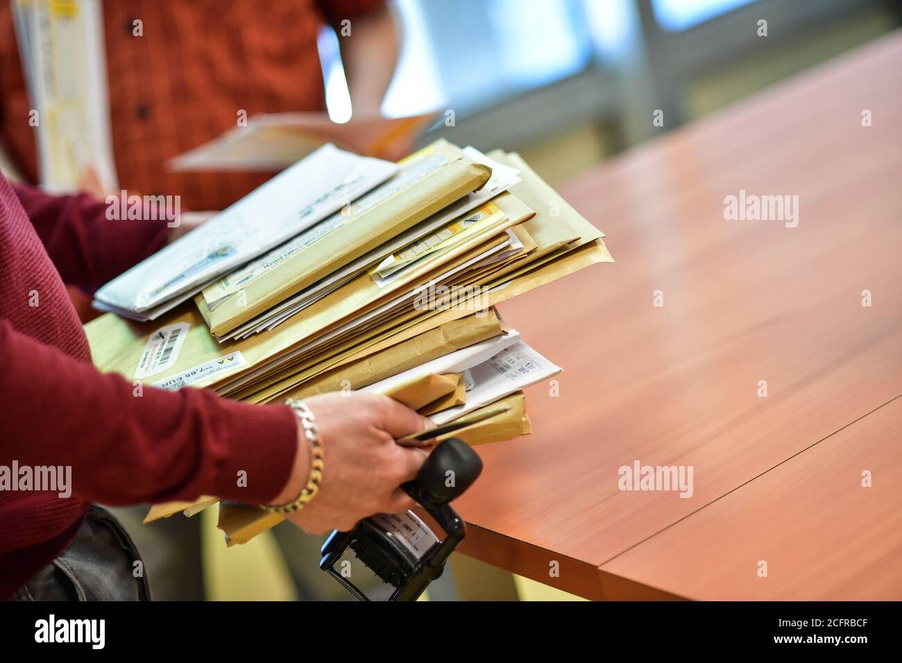 Servizio postale di un ente locale. Uomo che porta un mucchio di lettere, che sta per cadere su un tavolo Foto Stock